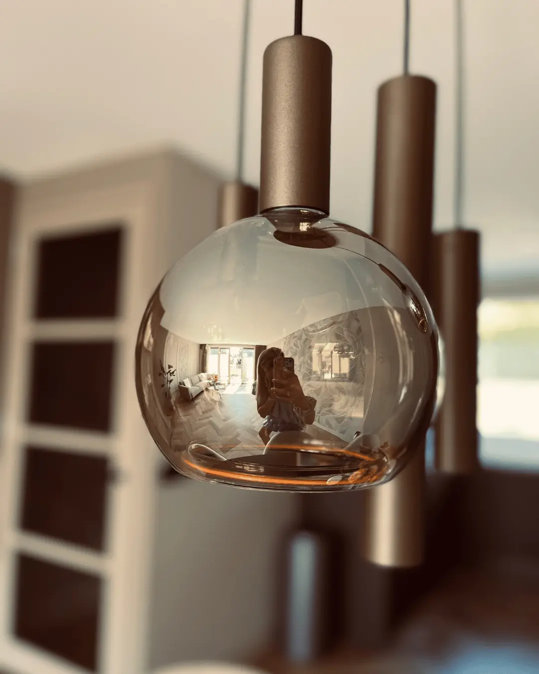 Close-up van een rookglazen bolhanglamp met bronskleurige cilinders erachter