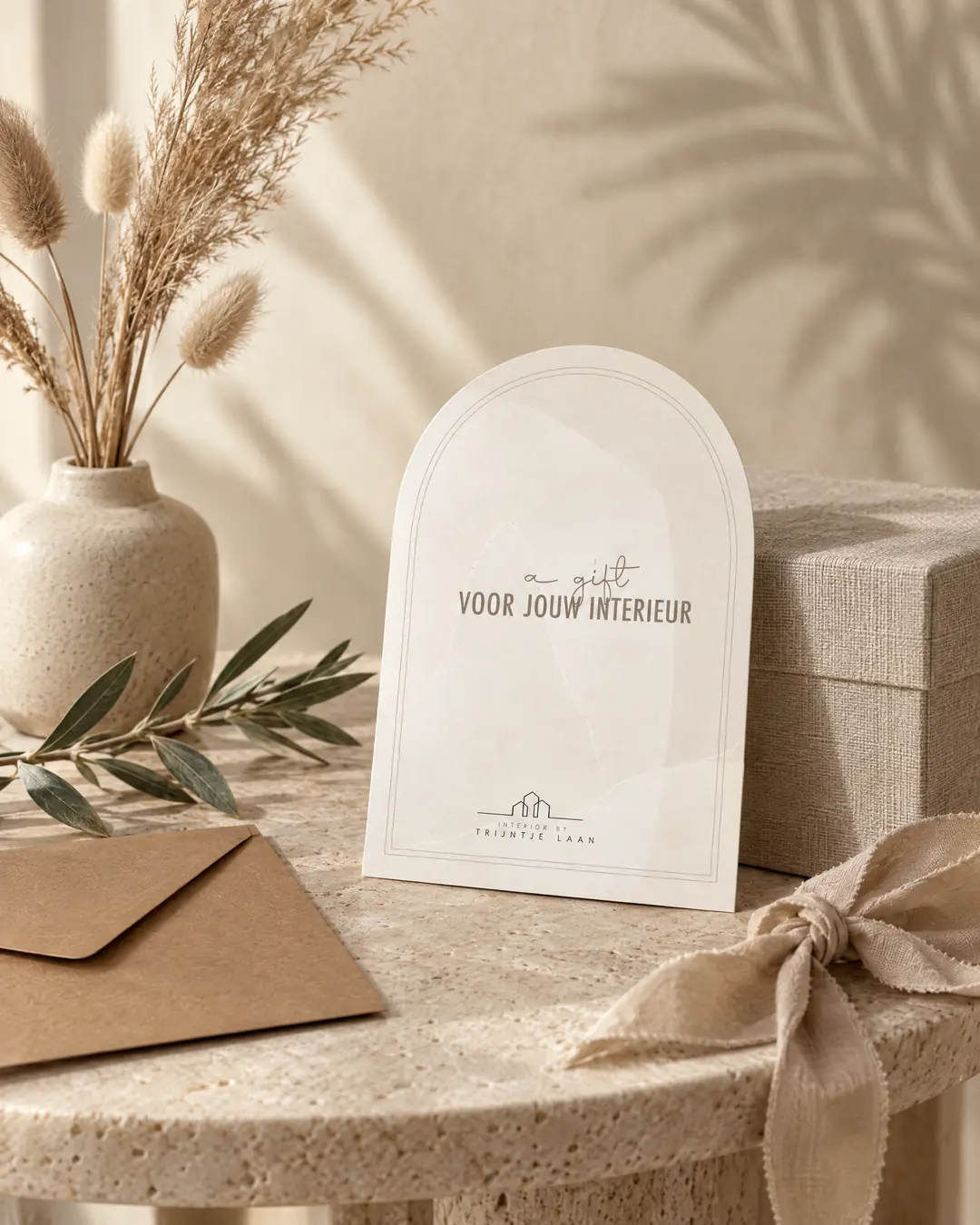 Giftcard van Interieurstudio Laan in boogvorm met de tekst Voor jouw interieur en het logo, op een travertin bijzettafel met droogbloemen, een envelop en een linnen strik