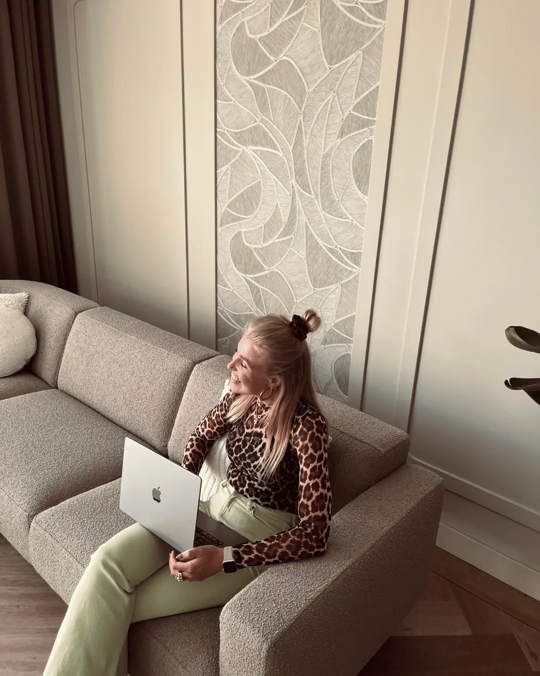 Trijntje Laan op een bank met laptop voor een behangpaneel
